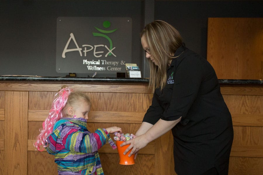 A healthcare worker hands out treats to a young girl with colorful hair at the reception of a physical therapy and wellness center in West Fargo.