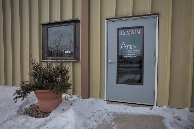 A quiet winter scene with a dusting of snow, featuring a barren shrub in a planter outside an industrial-style building in LaMoure with a door labeled 