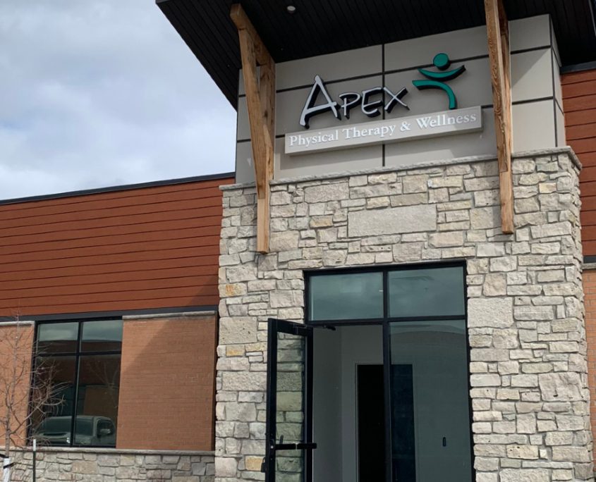 The exterior of Apex Physical Therapy & Wellness Center in South Fargo showcases its modern facade with stone and wood elements and a clear entrance door.