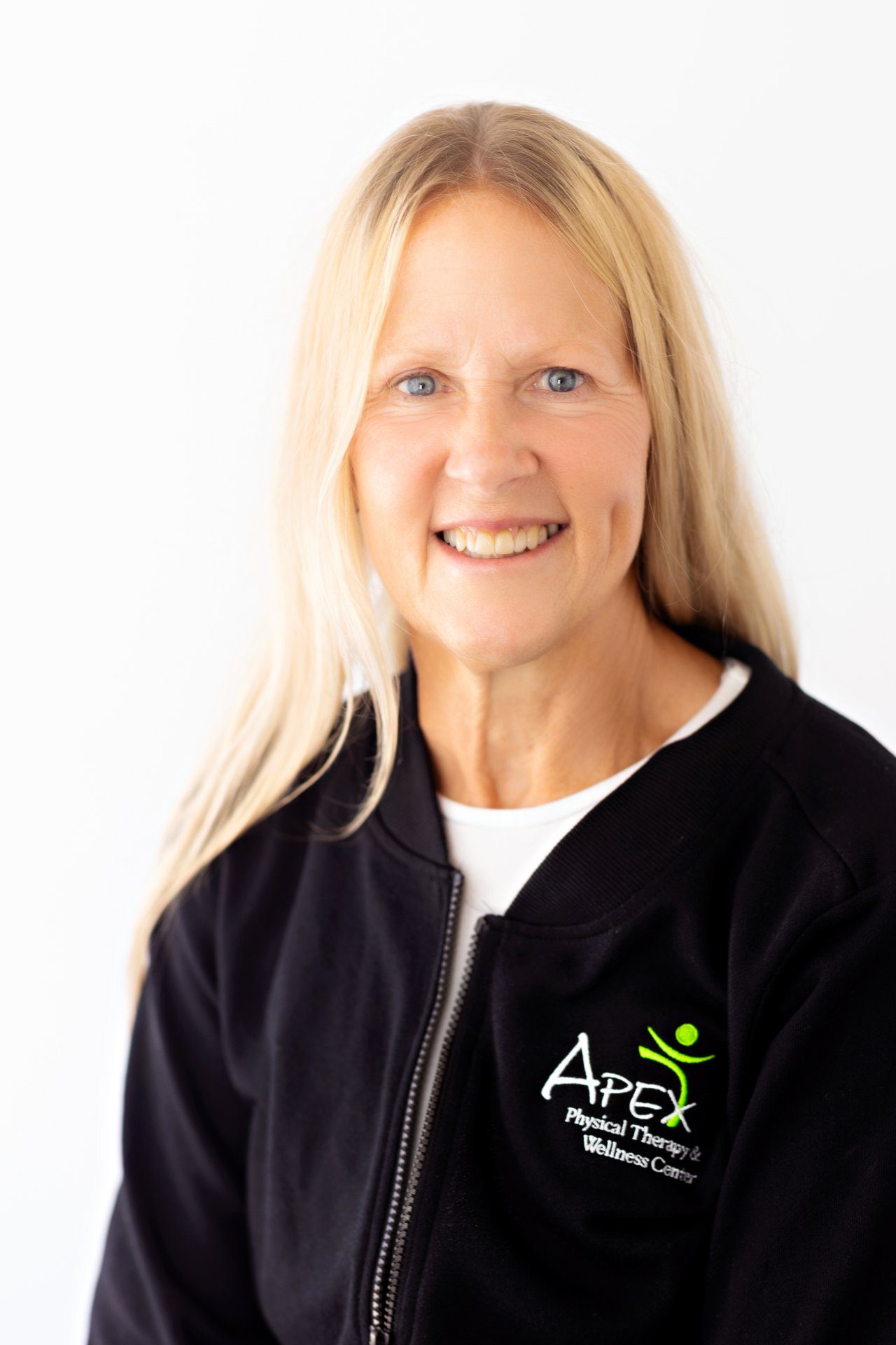 A professional portrait of Teresa Hanson smiling with blonde hair, wearing a black jacket with the Apex Physical Therapy & Wellness Center logo.