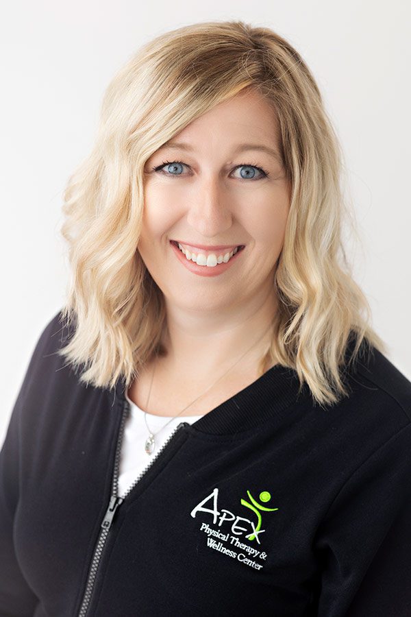 Professional headshot of a smiling woman with blonde hair, wearing a black jacket embroidered with the Kameron Ihry Hodem health and wellness center logo.