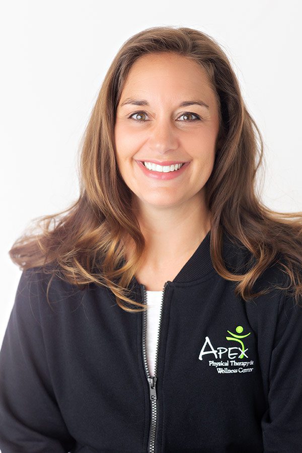 A smiling woman with long hair wearing a black zip-up jacket with an "Apex Physical Therapy & Wellness Center" logo, is identified as Brooke Erstad.