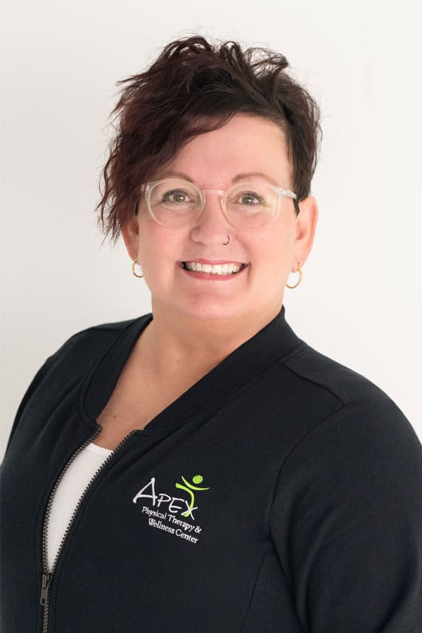 Beth Prashek, a professional woman with a warm smile wearing glasses and a black zip-up jacket with a company logo, stands against a white background.