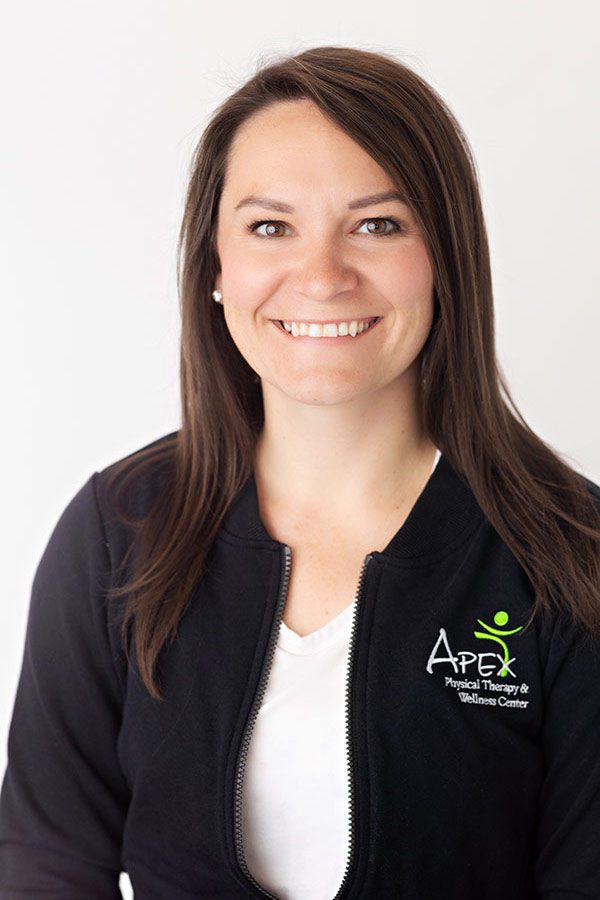 A professional portrait of Emma Neinaber smiling, wearing a black zip-up jacket with the logo "apex physical therapy & wellness center" embroidered on it.
