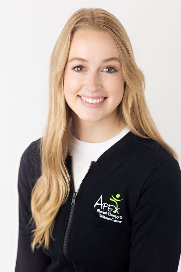 A smiling woman with long blonde hair wearing a black zip-up jacket with the "Josh Sorvig Apex Physical Therapy Center" logo embossed on the left side.