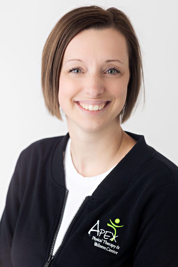 A professional portrait of a smiling woman named Emma Neinaber wearing a black jacket with an "Apex Physical Therapy & Wellness Center" logo on it.