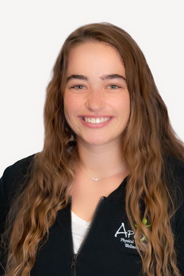 A cheerful woman named Jessica Christenson with long wavy hair, wearing a black zip-up jacket with a physical therapy and wellness logo, smiling against a white background.